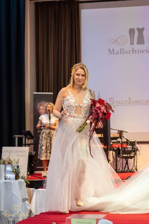 Bridal models displaying wedding gowns and bouquets on illuminated runway stage.