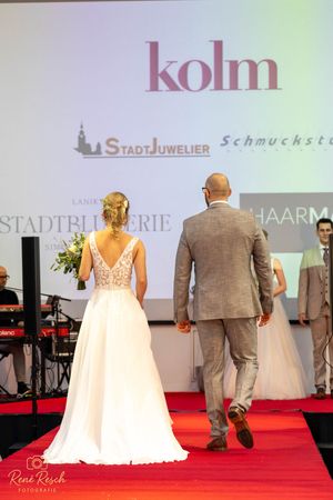 Bridal runway show displaying white wedding dresses and formal suits under professional lighting.