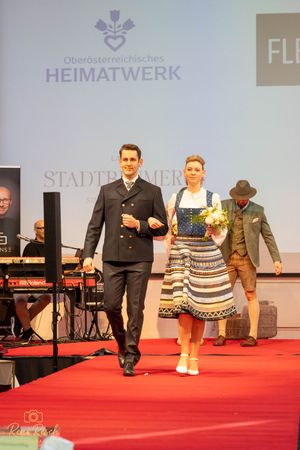Traditional Austrian fashion show featuring formal wear and dirndls on red carpet runway.