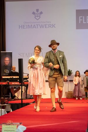 Fashion models wearing traditional Austrian attire walking runway under Heimatwerk banner.
