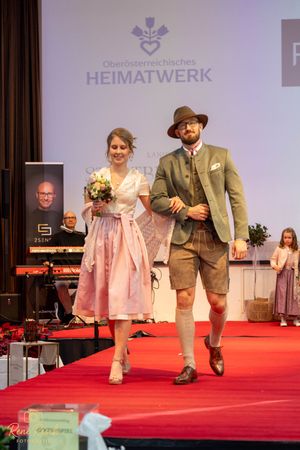 Traditional Austrian fashion show featuring dirndl dresses and lederhosen outfits on a red carpet runway.