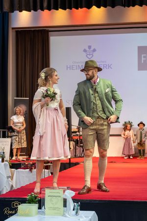 Models showcase traditional Bavarian clothing at the Heimatwerk fashion event on a red stage.
