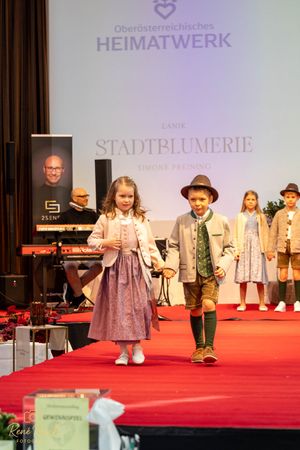 Children's fashion show displaying traditional Austrian folk costumes on a red runway.