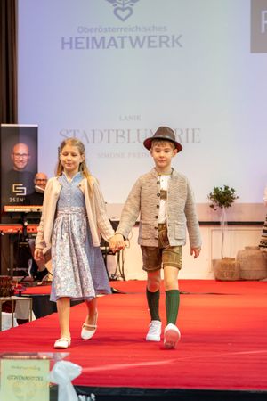 Fashion show featuring children in traditional Austrian dirndls and lederhosen on red carpet.