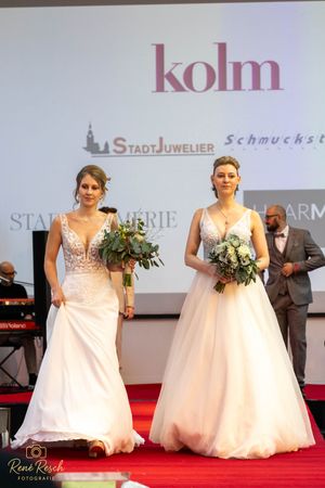 Models present wedding gowns with floral bouquets during a formal fashion show event.