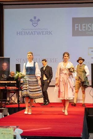 Traditional Austrian fashion show with models walking a red carpet runway.