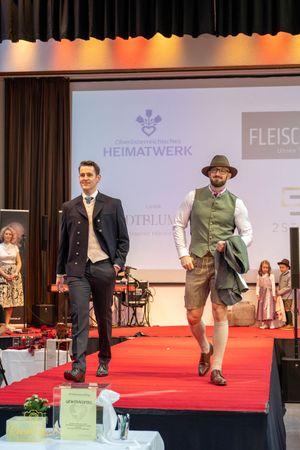 Models walking on red carpet stage showcasing traditional Alpine clothing and accessories.