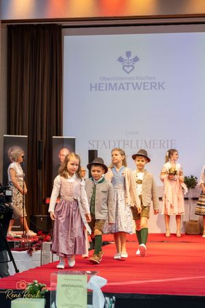 Group fashion show featuring traditional dirndls and folk costumes on red carpet runway.