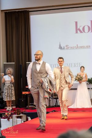 Fashion show models walk the runway in light-colored formal wear and wedding attire.