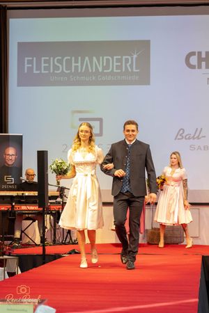 Fashion show finale featuring traditional Alpine clothing on illuminated red carpet stage.
