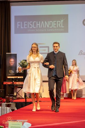 Models showcase traditional dirndl and tracht fashion on a red runway at a Fleischanderl fashion show.