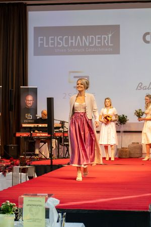 Model presents a traditional pink dirndl dress on red carpet runway with Fleischanderl branding.