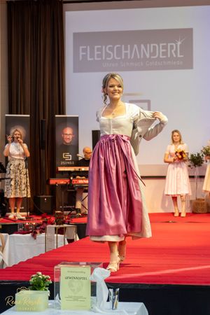 Traditional Austrian dirndl dress with pink skirt and cream top displayed on red carpet runway.