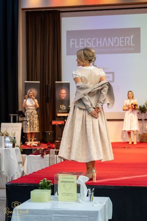 Model shows back view of cream colored dirndl dress on elevated runway platform.