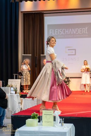 Side view of model in traditional dirndl with pink skirt and cream jacket on display platform.