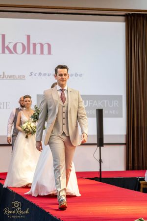 Formal wedding attire showcase on red carpet runway with light colored suits and white gowns.