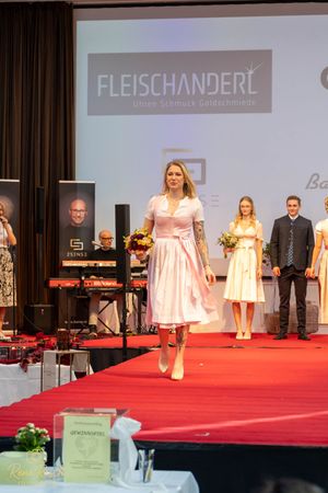 Fashion show featuring pink and cream dirndl dresses on red carpet runway with Fleischanderl branding.