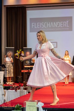 Model twirls in pink and white dirndl dress showcasing the full skirt on red carpet.