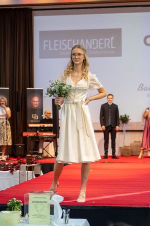 Young models in white dresses walk the red carpet at a formal fashion event.