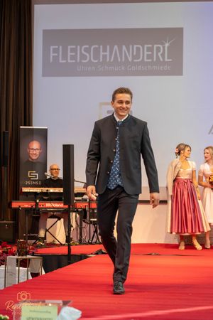 Model demonstrates suit on red carpet runway with Fleischanderl logo display.