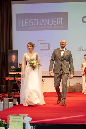 Bridal fashion show featuring white gowns and formal suits on red carpet runway.