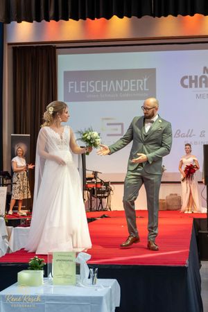 Models showcase bridal and formal wear on red carpet runway with stage lighting.