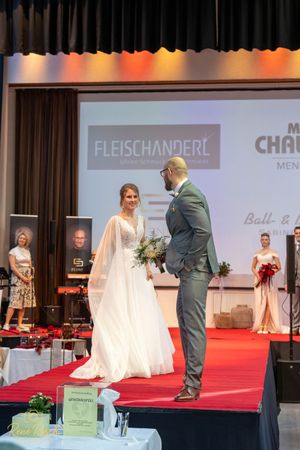 Wedding fashion show with models displaying bridal gowns and suits on red carpet.