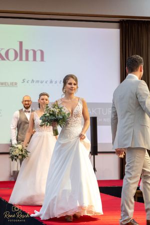 Wedding fashion show featuring multiple models in white gowns and formal suits on red carpet.