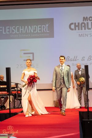 Fashion show featuring bridal gowns and formal wear on illuminated red carpet runway.