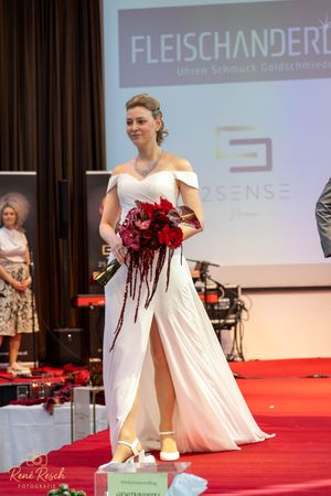 Models present wedding dresses with red floral bouquets on fashion runway.