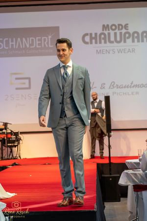 Men's formal wear collection displayed on red carpet runway with branded backdrop.