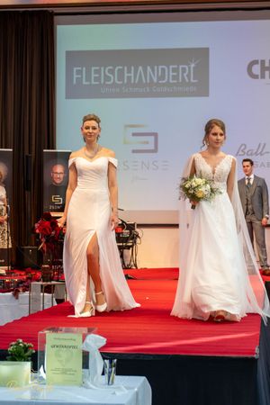 Models showcase elegant white wedding gowns on a red carpet runway at a bridal fashion show.