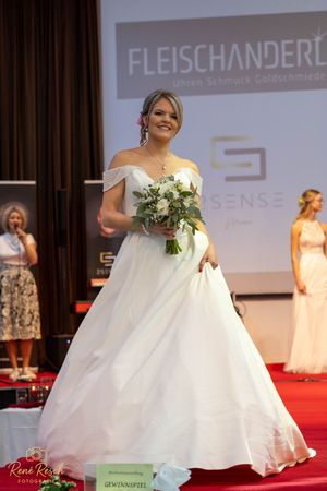 Bridal fashion show featuring flowing white wedding dresses with floral bouquets on red carpet.