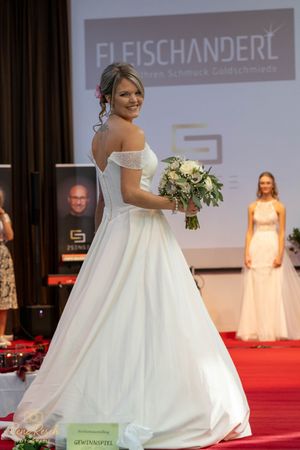 Wedding gowns with full skirts and bouquets displayed during a bridal fashion show.