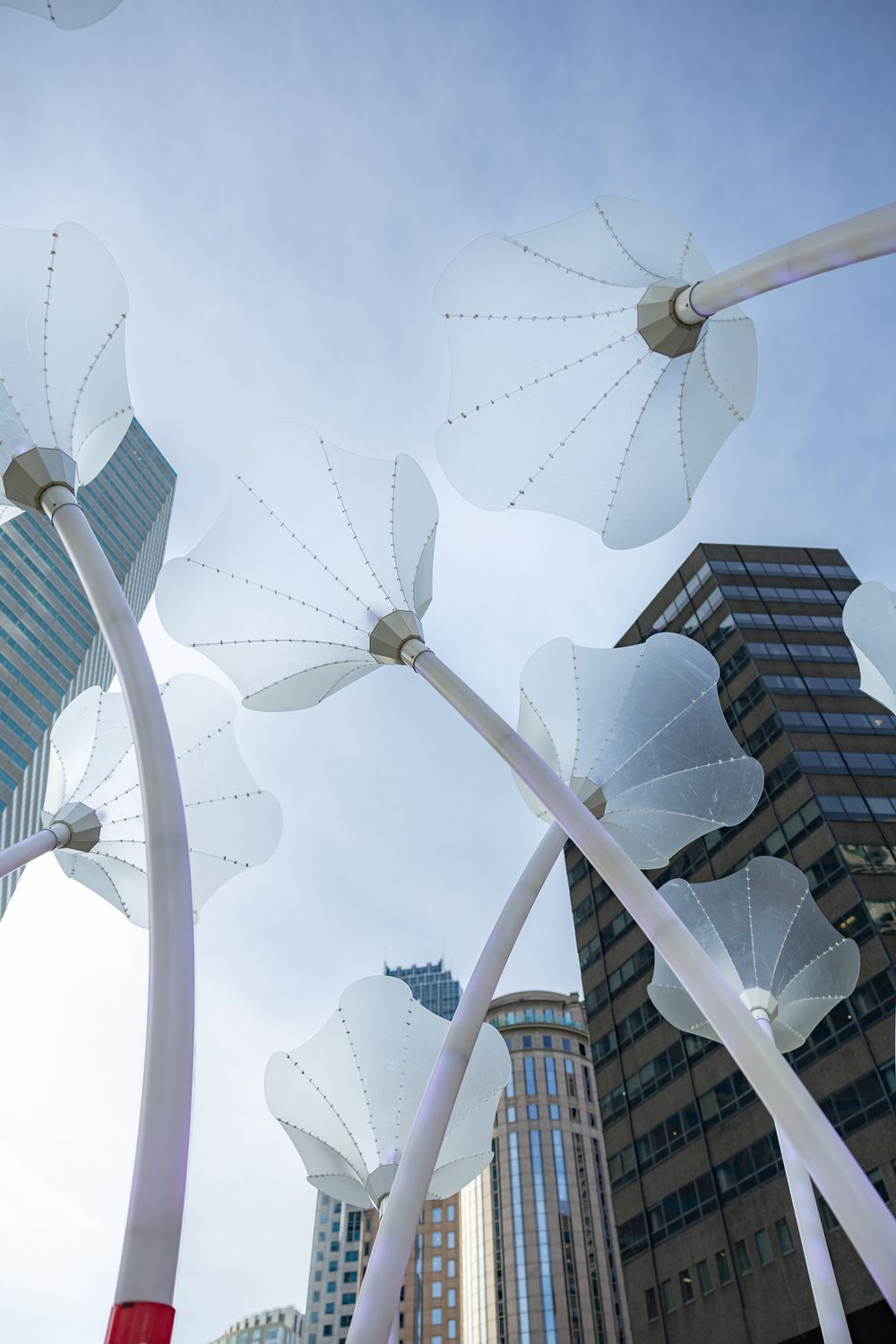 Large white kinetic sculptures with wing-like panels move against a backdrop of modern office buildings and blue sky.