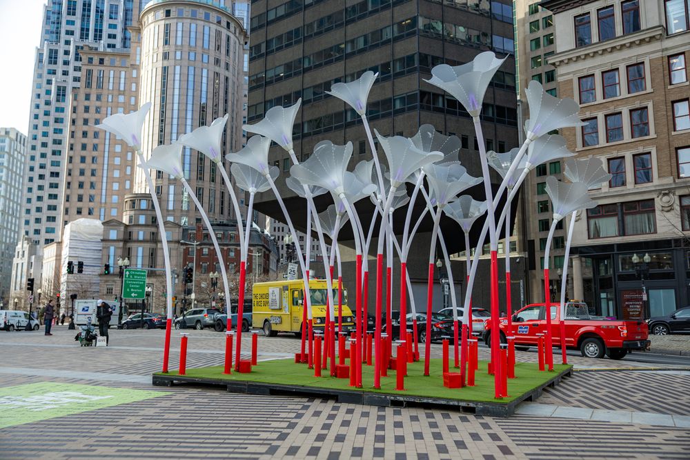 Colorful art installation featuring red and silver metal sculptures in an urban plaza surrounded by tall buildings.