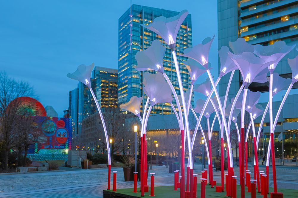Illuminated LED light poles with red bases create a futuristic outdoor art installation against a twilight urban skyline.