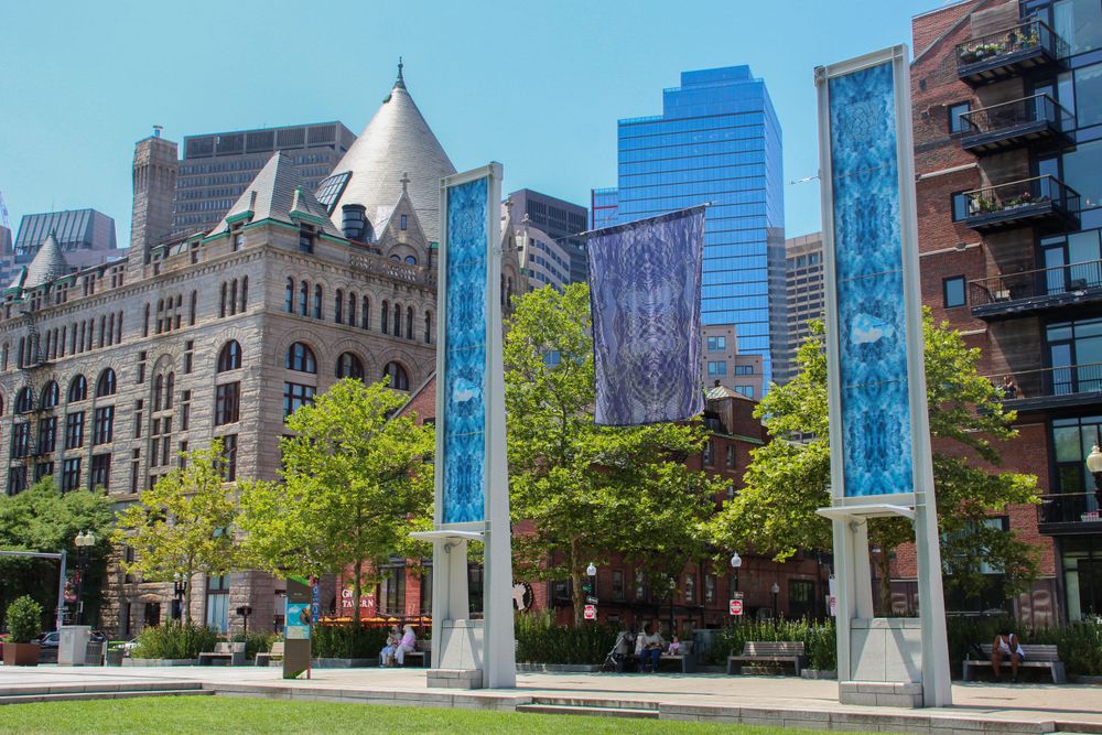 Historic architecture and modern skyscrapers frame blue art installations in an urban plaza.