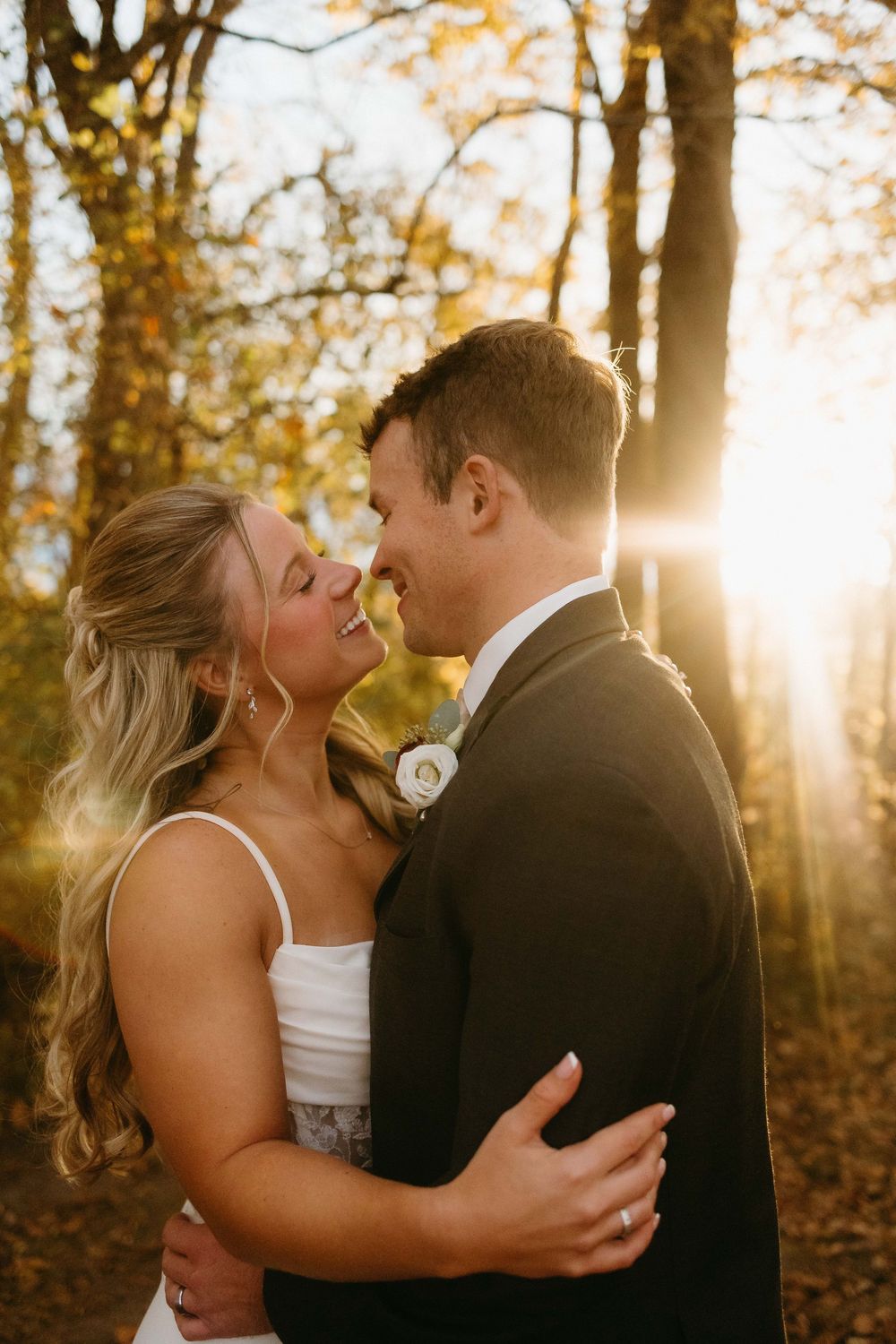 A romantic wedding couple embraces in a sun-drenched autumn forest with golden light filtering through the trees.