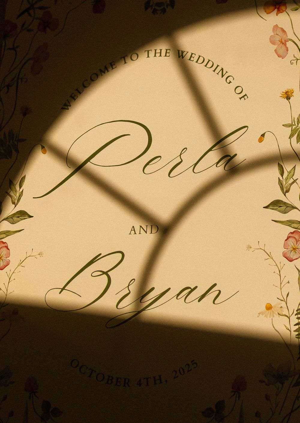 Elegant wedding invitation with calligraphy names Perla and Bryan surrounded by floral designs in warm lighting.