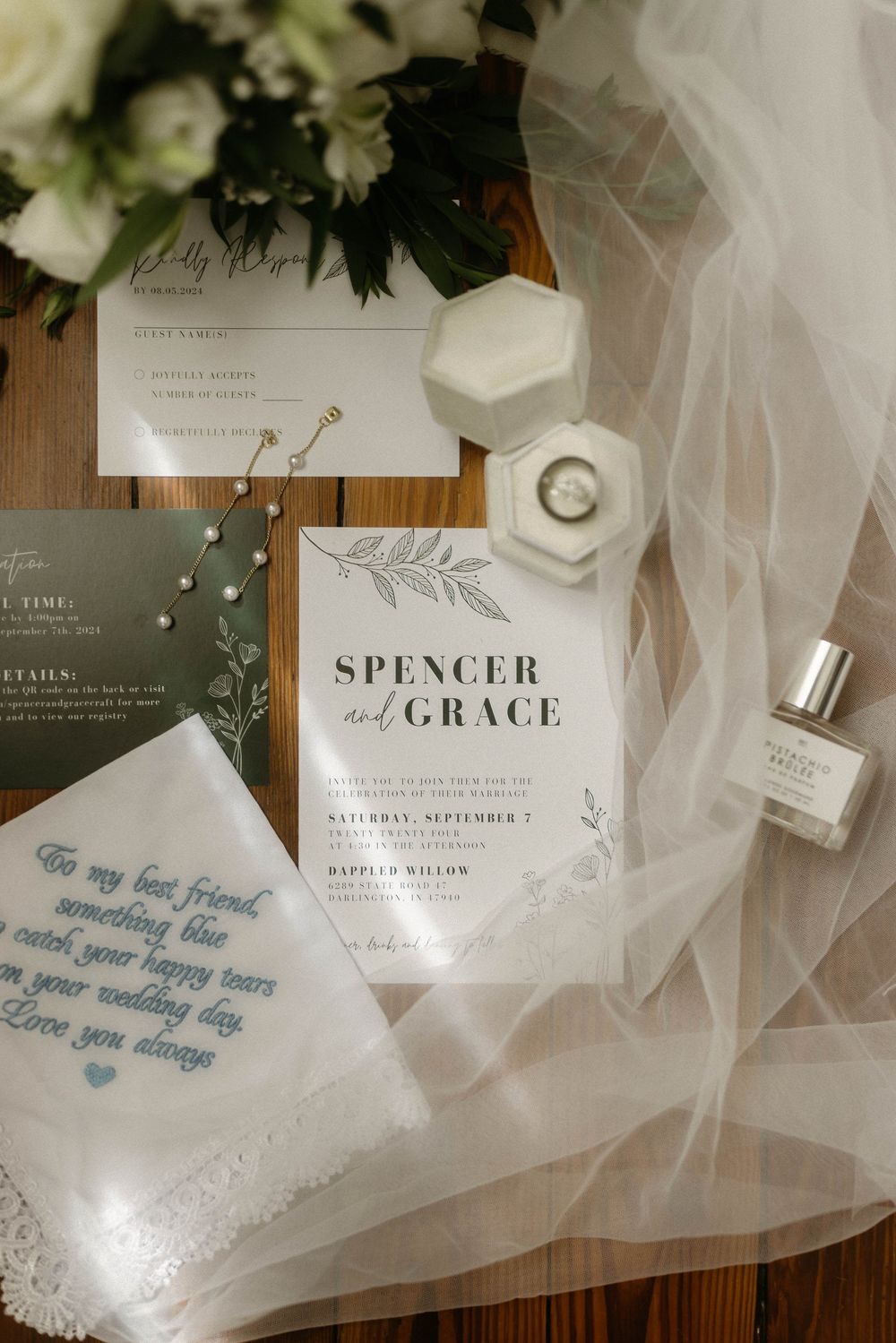 Elegant wedding invitation suite with white tulle veil and floral accents laid out on dark wooden surface.