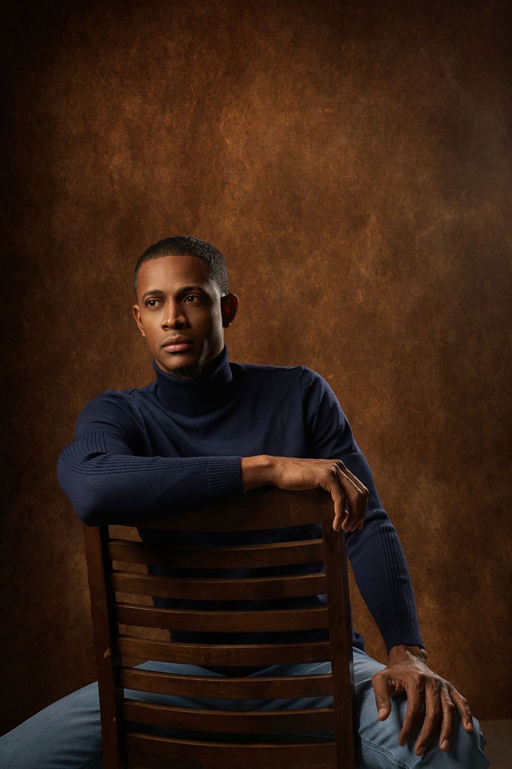 Portrait series against brown backdrop showing person in navy sweater posing on wooden chair from different angles.