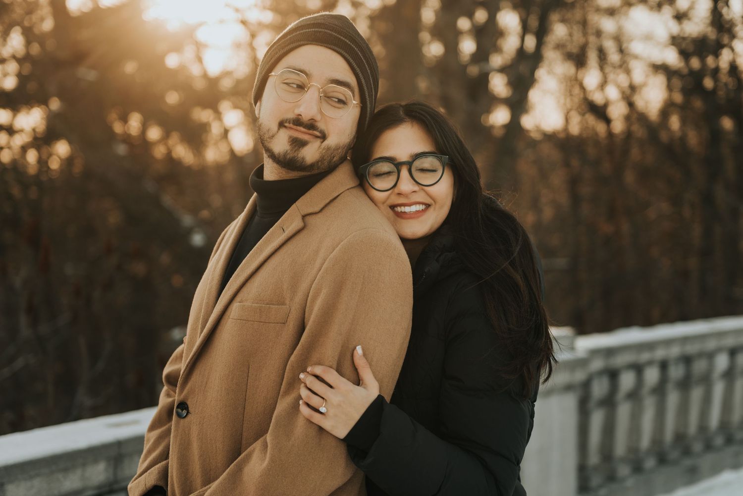 A couple embraces during golden hour sunset on a bridge while wearing casual fall attire.