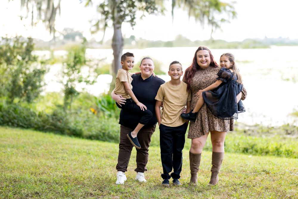 A group of people standing together and smiling on a grassy hill overlooking a waterfront on a bright day.