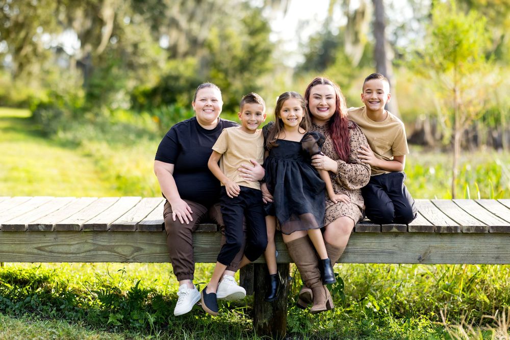 Family group sitting together outdoors on grassy hill during golden hour sunset photography session.