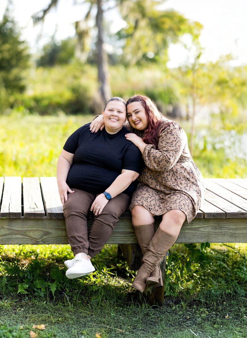 A couple sits together on a wooden boardwalk surrounded by lush greenery in a romantic outdoor photoshoot.