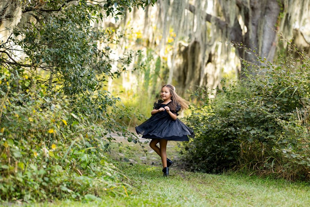 A ballerina dances gracefully through a sunlit garden with Spanish moss hanging from trees in the background.