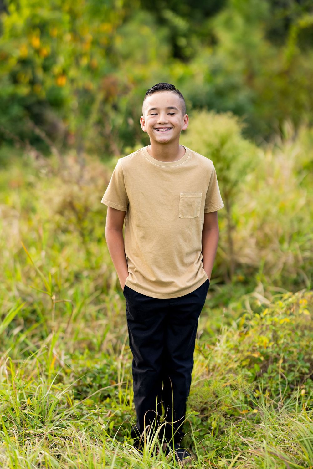 A joyful moment captured in tall grass and wildflowers on a sunny day wearing a tan t-shirt and dark pants.