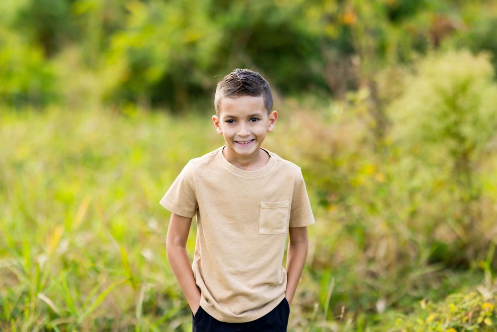 A child wearing a tan t-shirt and dark pants runs and plays outdoors in a lush green natural setting.