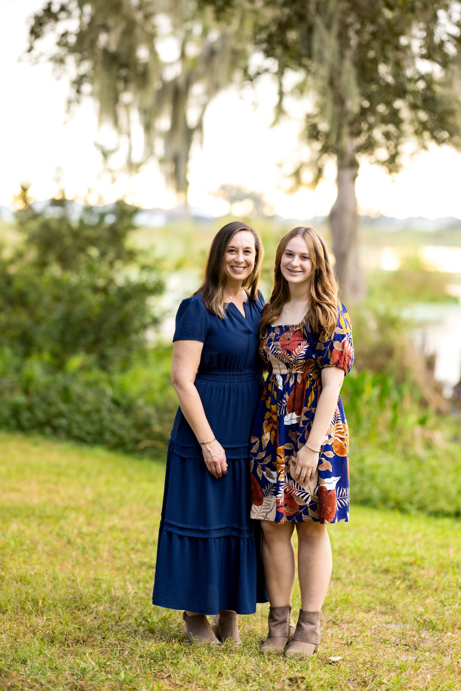 Two women stand together outdoors in coordinating navy and floral outfits against a natural backdrop.